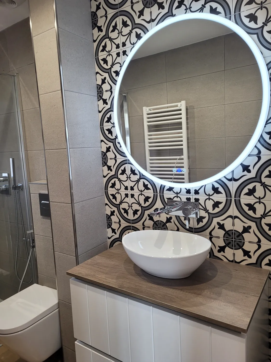 Baño reformado con espejo circular retroiluminado y azulejo hidráulico