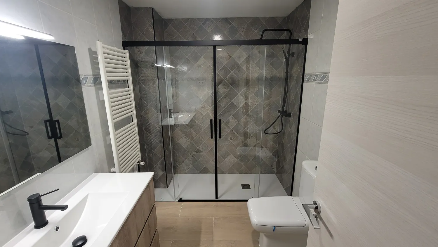 Baño reformado en tonos grises con mampara de perfil negro