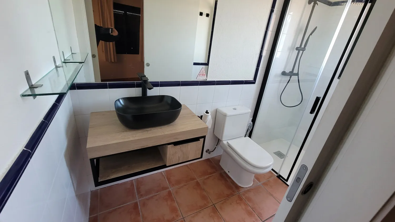 Baño reformado con lavabo sobre encimera de madera y mampara negra